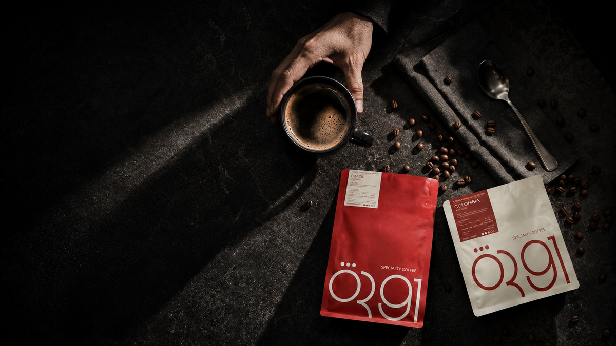 Red and white OR91 specialty coffee bags beside a cup of coffee